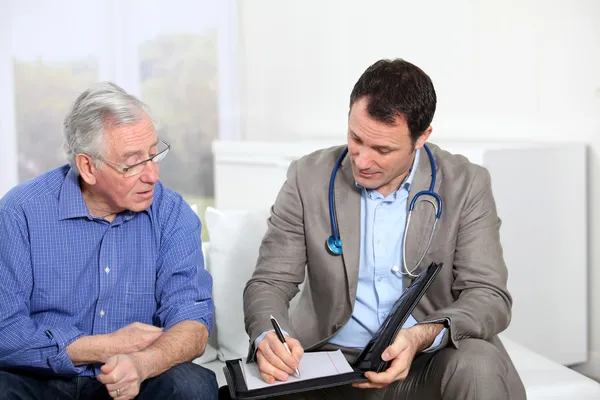 Médico que escreve prescrição médica para o homem idoso — Fotografia de Stock