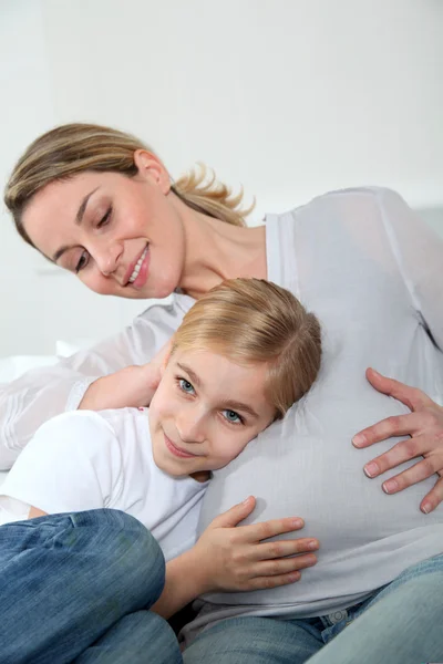 Little blonde girl listening to pregnant woman belly — Stock Photo, Image