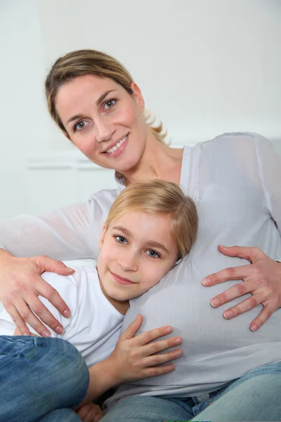 Little blonde girl listening to pregnant woman belly — Stock Photo, Image