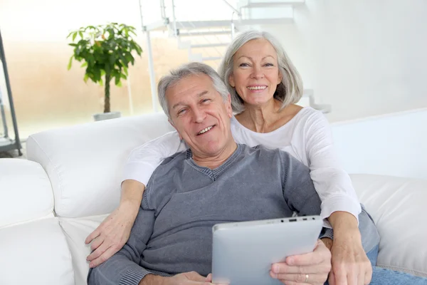 Ανώτερος ζευγάρι, κάθεται σε καναπέ με ηλεκτρονικό, ταμπλετών — Φωτογραφία Αρχείου