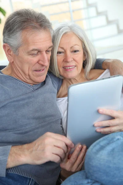 Starší pár sedící v pohovce s elektronickým tablet — Stock fotografie