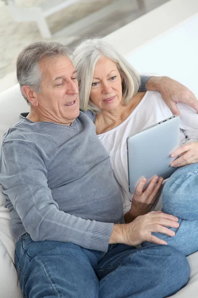 Старшая пара сидит на диване с электронным планшетом — стоковое фото