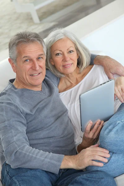 Starší pár sedící v pohovce s elektronickým tablet — Stock fotografie