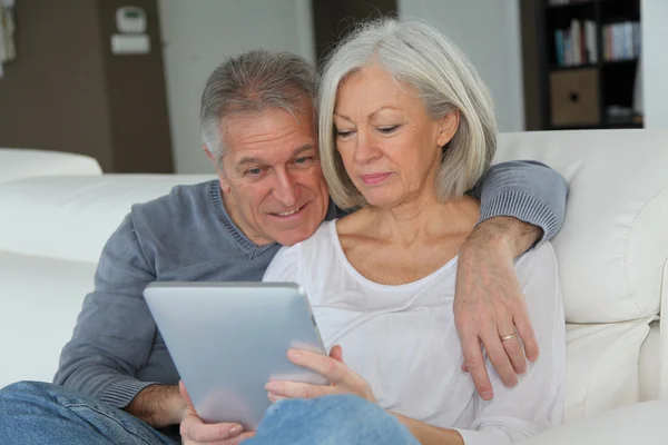 Senior couple sitting in sofa with electronic tablet — Stock Photo, Image