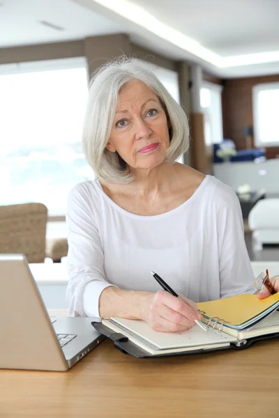 Senior woman at home writing on agenda — Stock Photo, Image