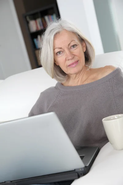 Mujer mayor que se relaja en casa delante de la computadora portátil —  Fotos de Stock
