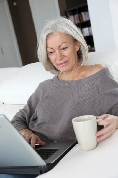 Femme âgée se détendre à la maison devant un ordinateur portable — Photo