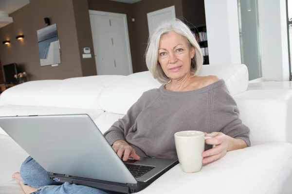 Donna anziana rilassante a casa davanti al computer portatile — Foto Stock