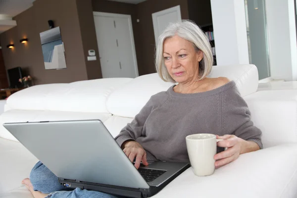 Ανώτερος γυναίκα χαλάρωση στο σπίτι μπροστά από το φορητό υπολογιστή — Φωτογραφία Αρχείου