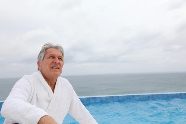 Hombre mayor sentado junto a la piscina — Foto de Stock