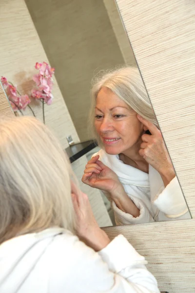 Donna anziana che applica crema idratante sul viso — Foto Stock