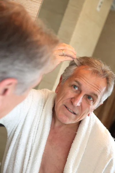 Starší muž při pohledu na vlasy v zrcadle — Stock fotografie