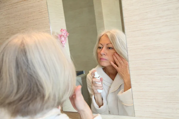 Donna anziana che applica crema idratante sul viso — Foto Stock