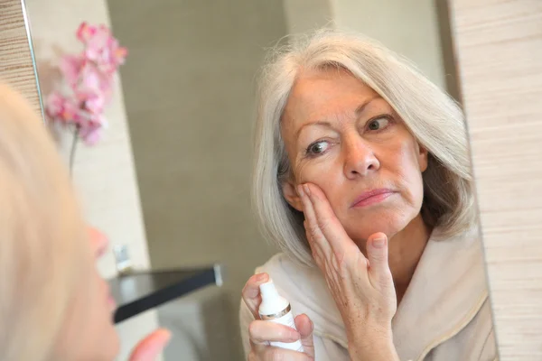 Senior woman applying moisturizer on her face — Stock Photo, Image