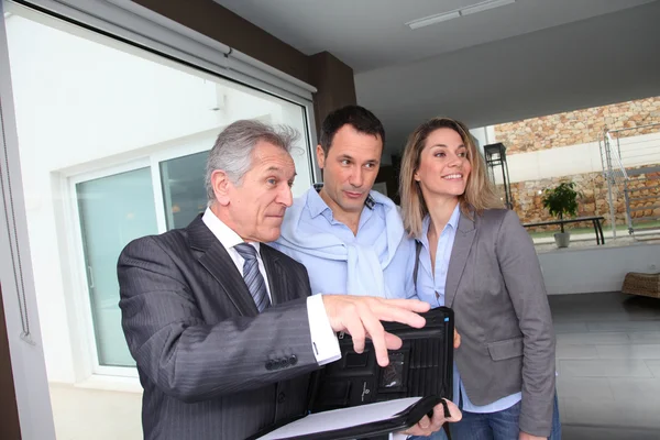 Real estate agent showing modern house to couple Stock Picture