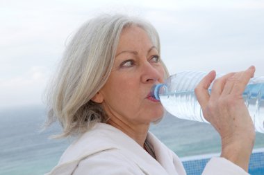 Senior woman dinking water from bottle clipart