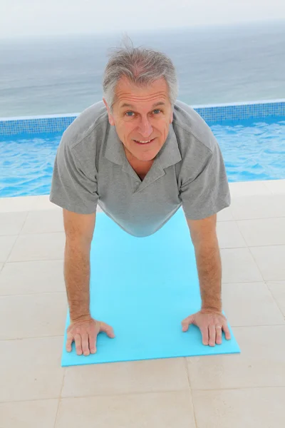 Homem sênior fazendo exercícios por uma piscina — Fotografia de Stock