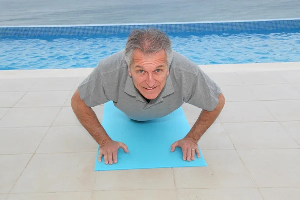 Homem sênior fazendo exercícios por uma piscina — Fotografia de Stock