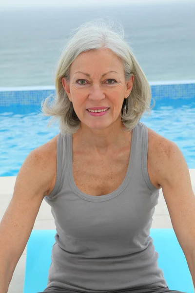 Mulher sênior fazendo exercícios por uma piscina — Fotografia de Stock