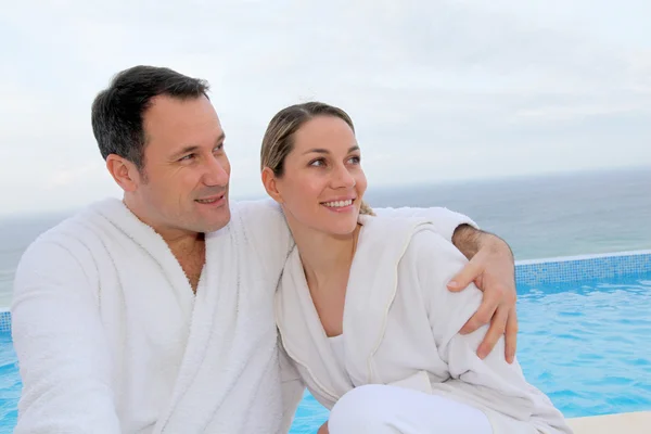 Couple in bathrobe sitting by swimming-pool — Stock Photo, Image