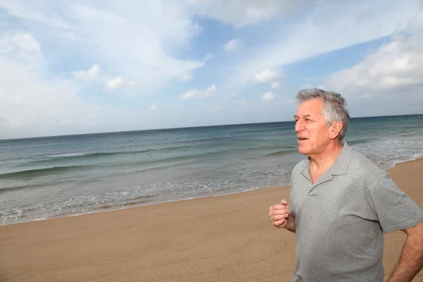 Senior man loopt op het strand — Stockfoto