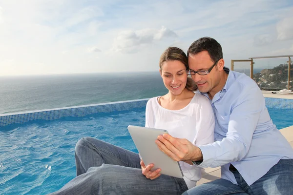 Happy couple using electronic tablet by swimming-pool — Stock Photo, Image