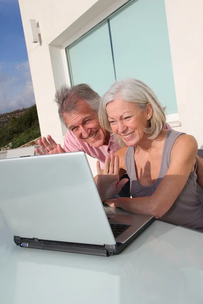 ラップトップ コンピューターにウェブカメラで手を振っている年配のカップル — ストック写真