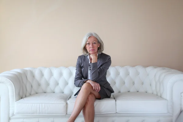 Старша жінка сидить у білому дивані — стокове фото
