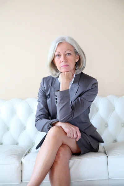 Äldre kvinna sitter i vita soffa — Stockfoto