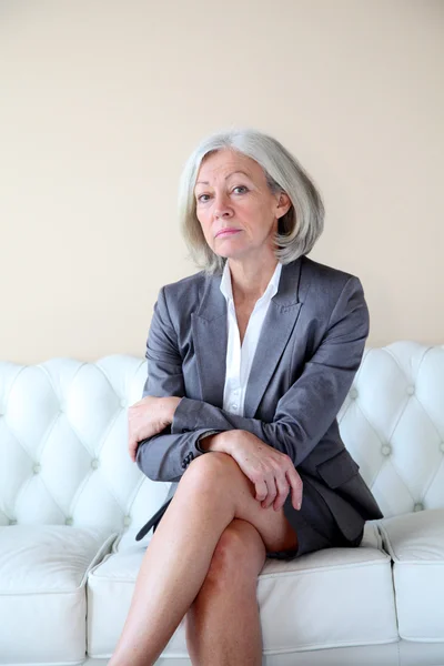 Senior mulher sentada no sofá branco — Fotografia de Stock
