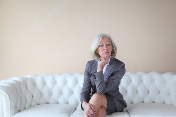 Seniorin sitzt auf weißem Sofa — Stockfoto