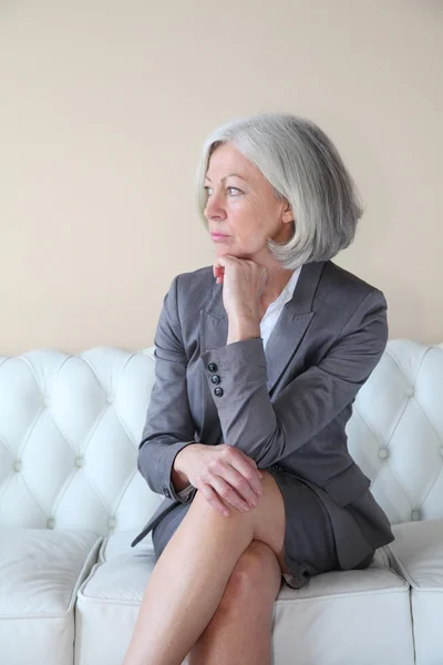 Senior vrouw zitten in witte Bank — Stockfoto
