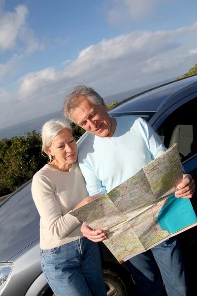 Старшая пара смотрит на дорожную карту на автомобильном капоте — стоковое фото