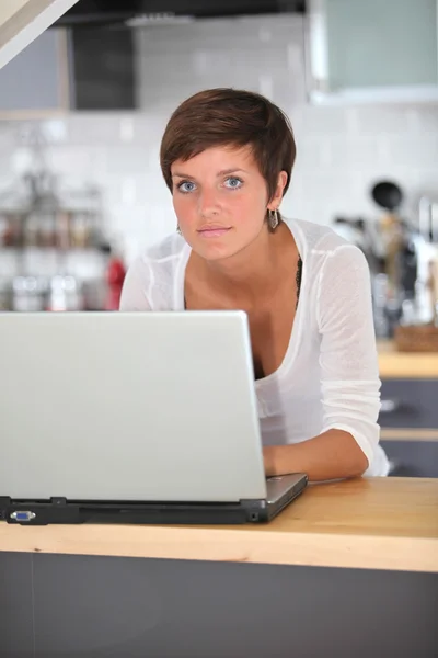 Jonge vrouw in keuken met laptopcomputer — Stockfoto