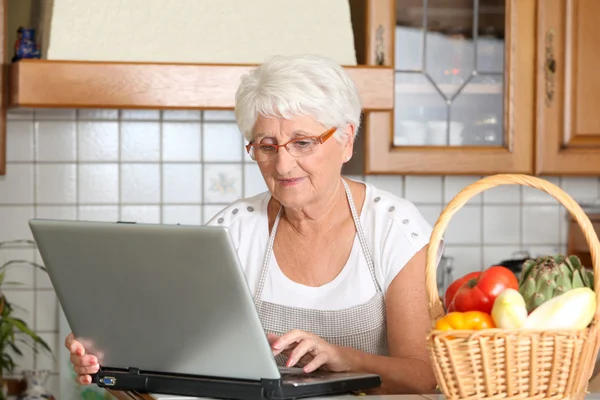 Donna anziana in cucina con computer portatile — Foto Stock