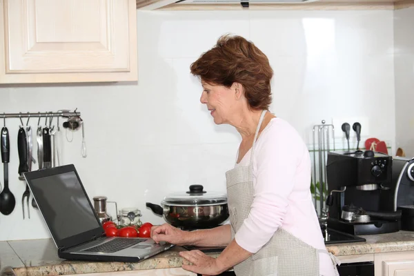 Старшая женщина на кухне с ноутбуком — стоковое фото