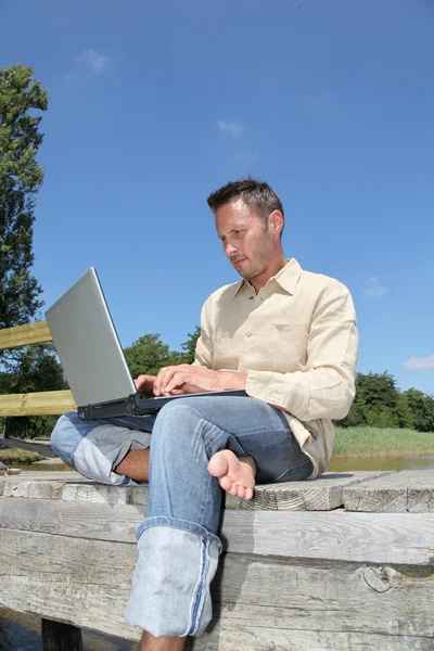 Uomo con computer portatile su un pontone — Foto Stock