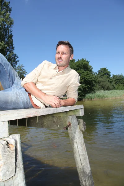Hombre descansando en un pontón junto a un lago — Foto de Stock