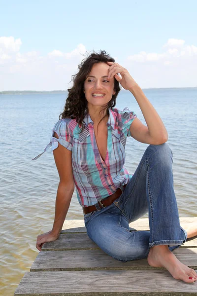 Mujer sentada en un pontón junto a un lago — Foto de Stock