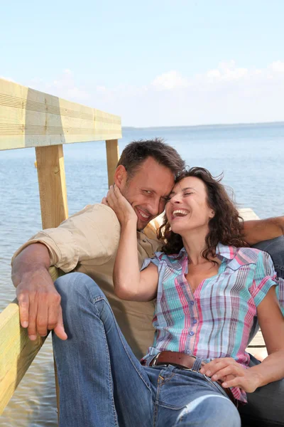 Loving couple sitting on a pontoon by a lake — Stock Photo, Image