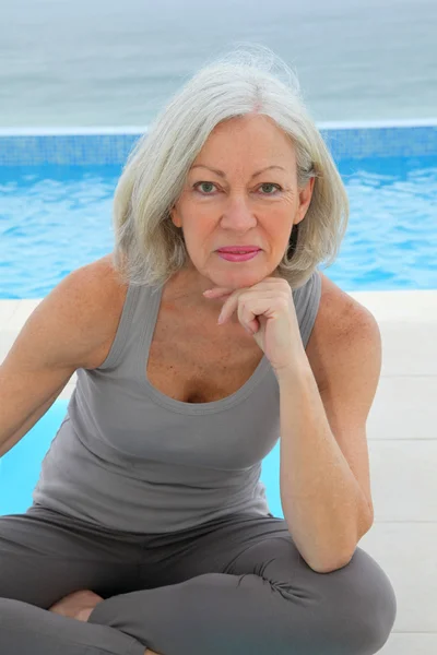 Senior woman doing exercises by a swimming-pool — Stock Photo, Image