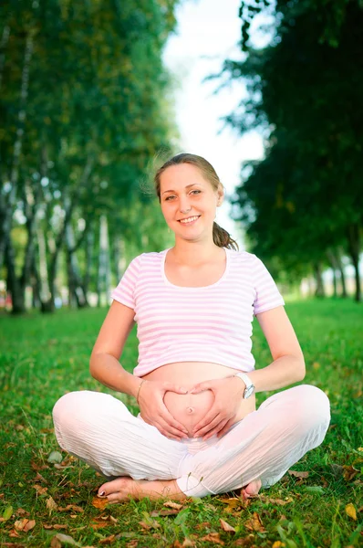 Mulher grávida bonita mostra um coração — Fotografia de Stock