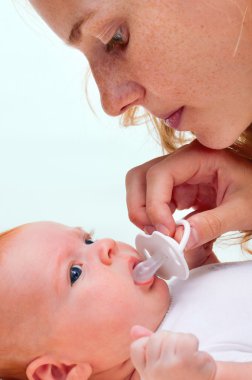 Young mother trying to give baby`s dummy to her newborn baby clipart