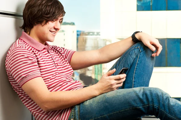 Uśmiechający się modny młody chłopak pisania wiadomości na telefon komórkowy — Zdjęcie stockowe