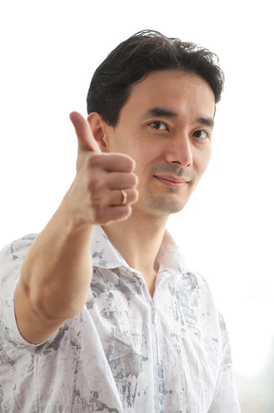 Portrait of a young guy standing against bright window showing thumb up si — Stock Photo, Image