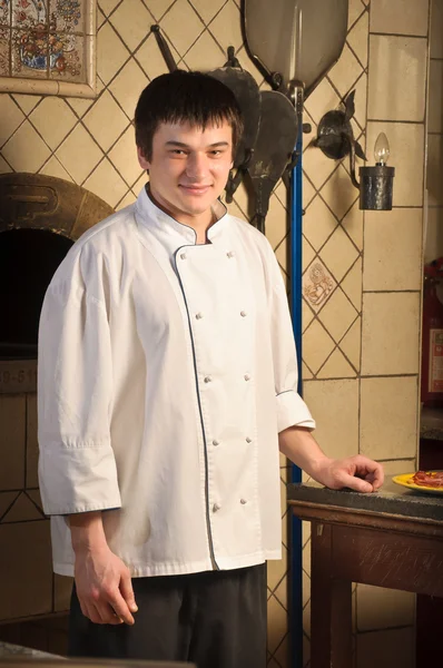 Um jovem chef de pé ao lado do forno — Fotografia de Stock