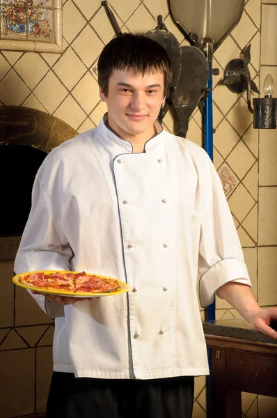 Um jovem chef de pé ao lado do forno — Fotografia de Stock