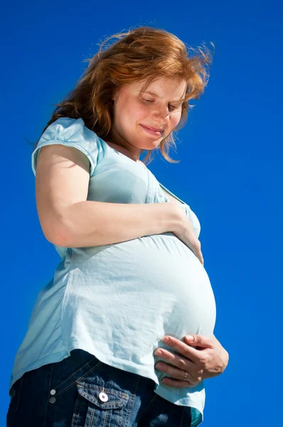 Schöne schwangere Frau schaut auf ihren Bauch — Stockfoto