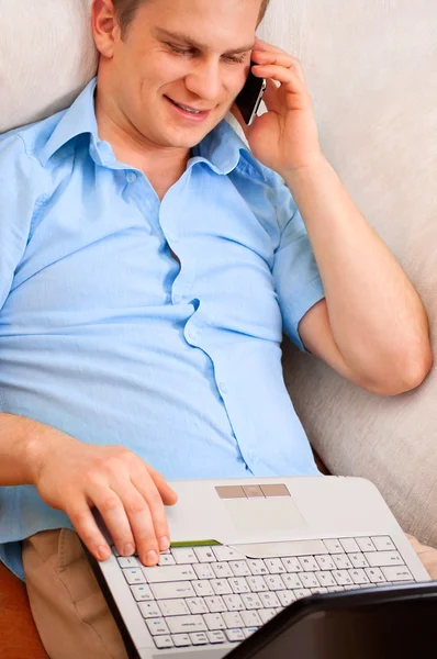 ハンサムな男のソファで横になっている電話に笑みを浮かべてください。 — ストック写真