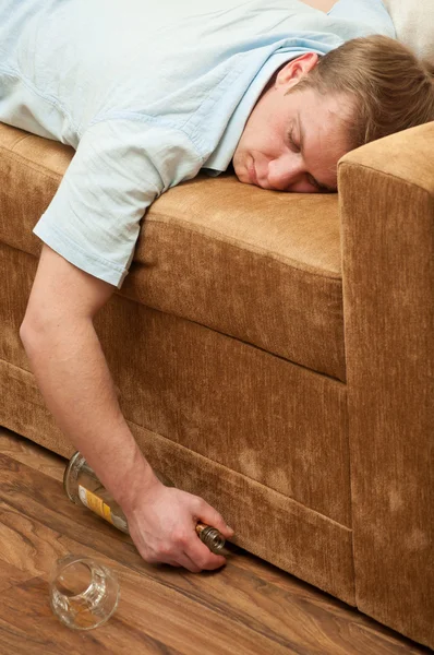 一个年轻人在沙发上睡着威士忌一瓶 — 图库照片